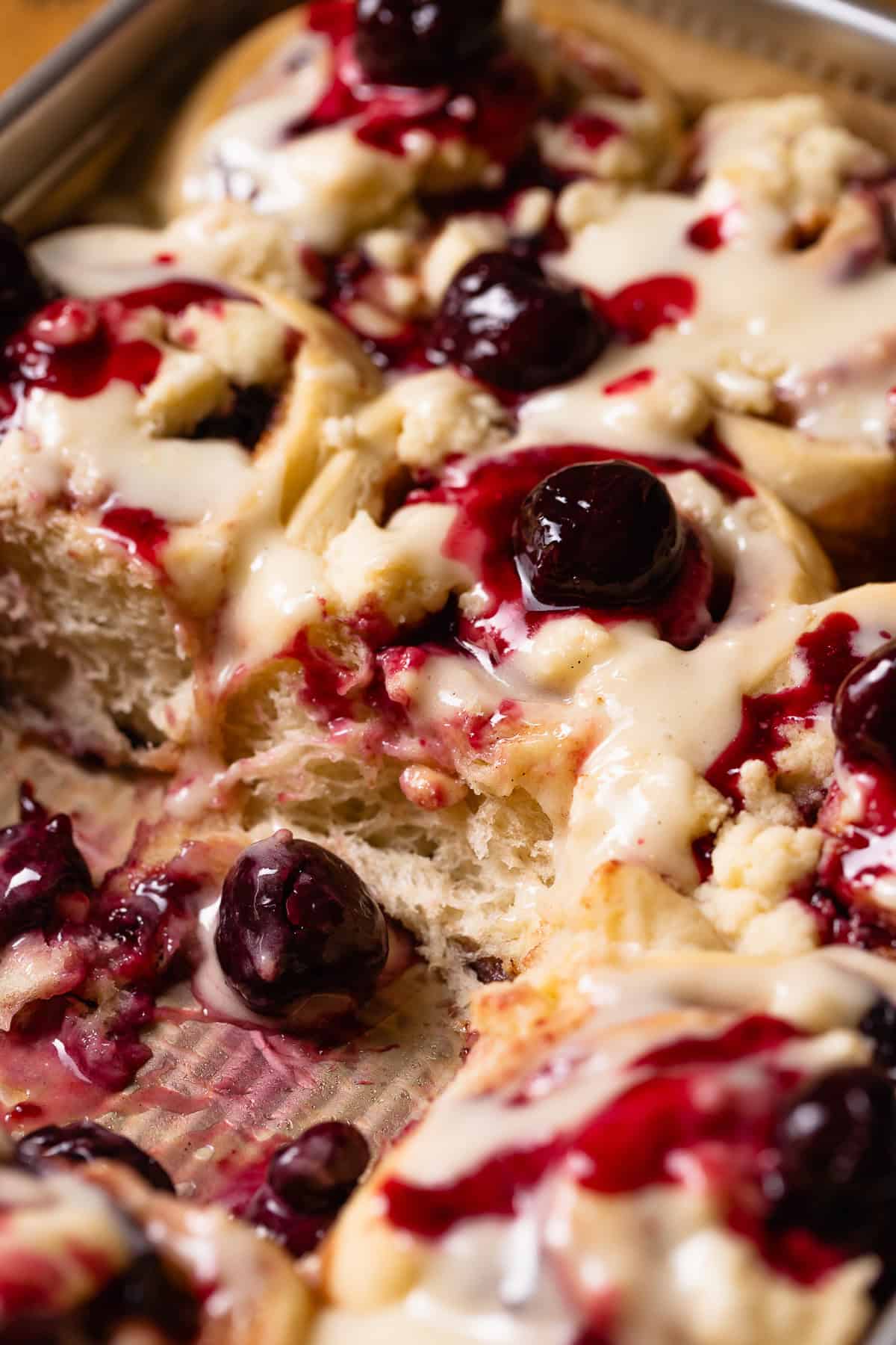 Cherry pie cinnamon rolls in a baking pan, swirled with cherry filling and topped with pie crumb.