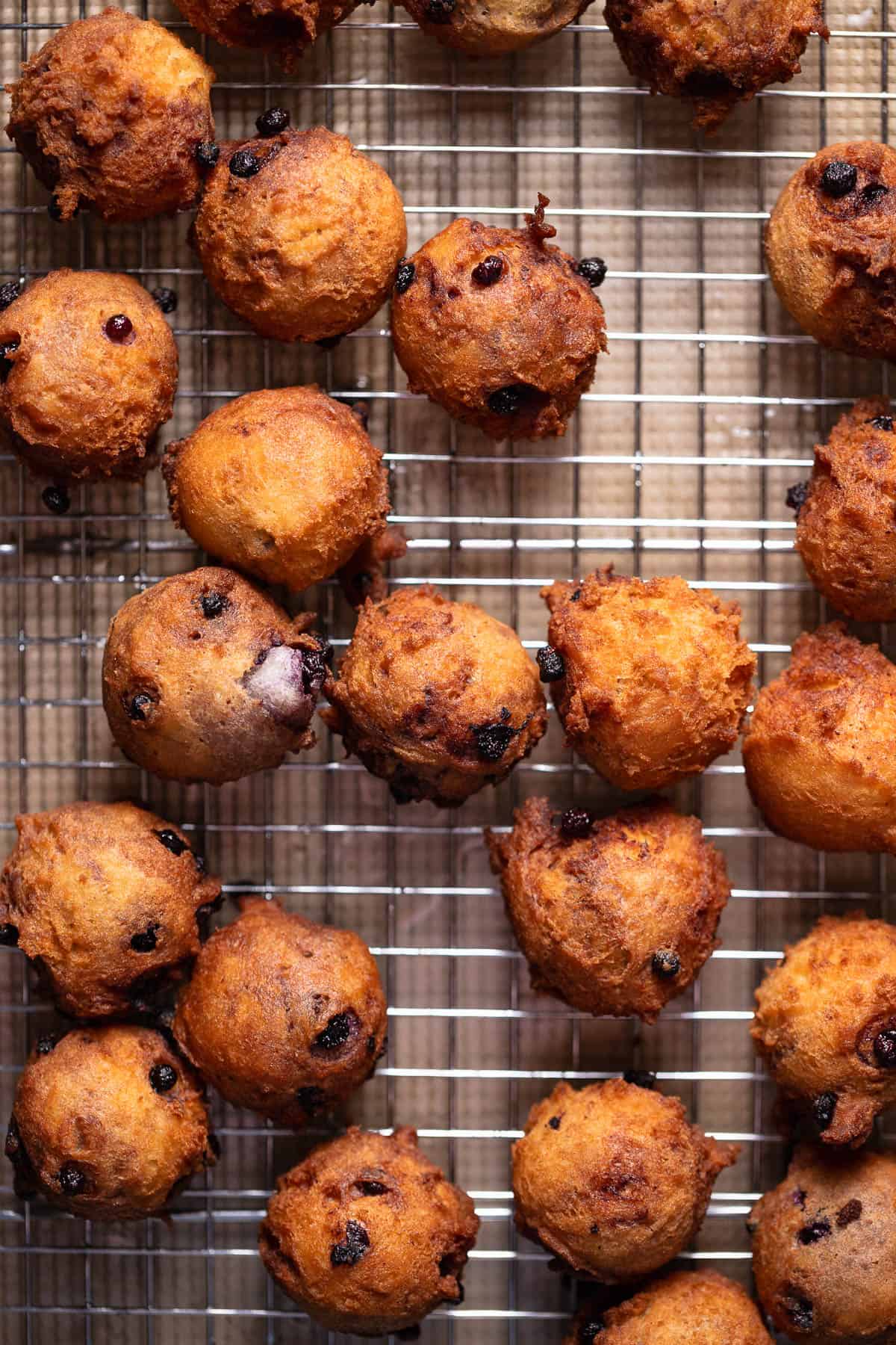 Mini blueberry donuts fried to golden brown on a wire rack cooling.