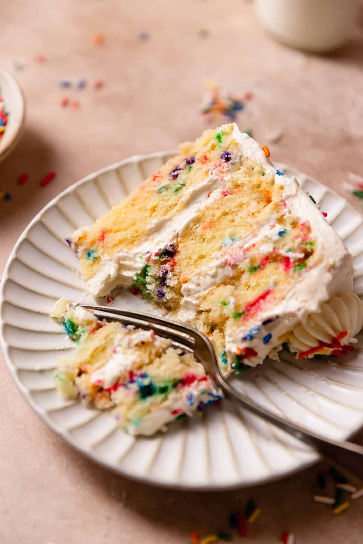 A slice of funfetti cake on a plate with a fork digging into a bite.
