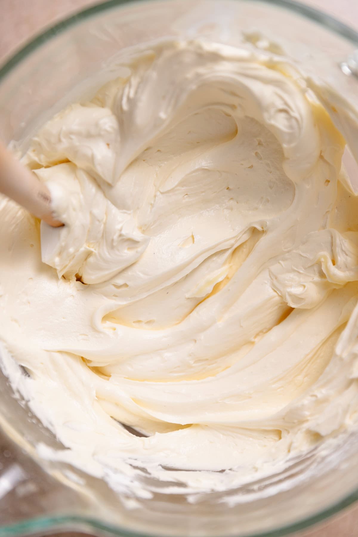 Vanilla buttercream frosting in a glass mixer bowl with a spatula.