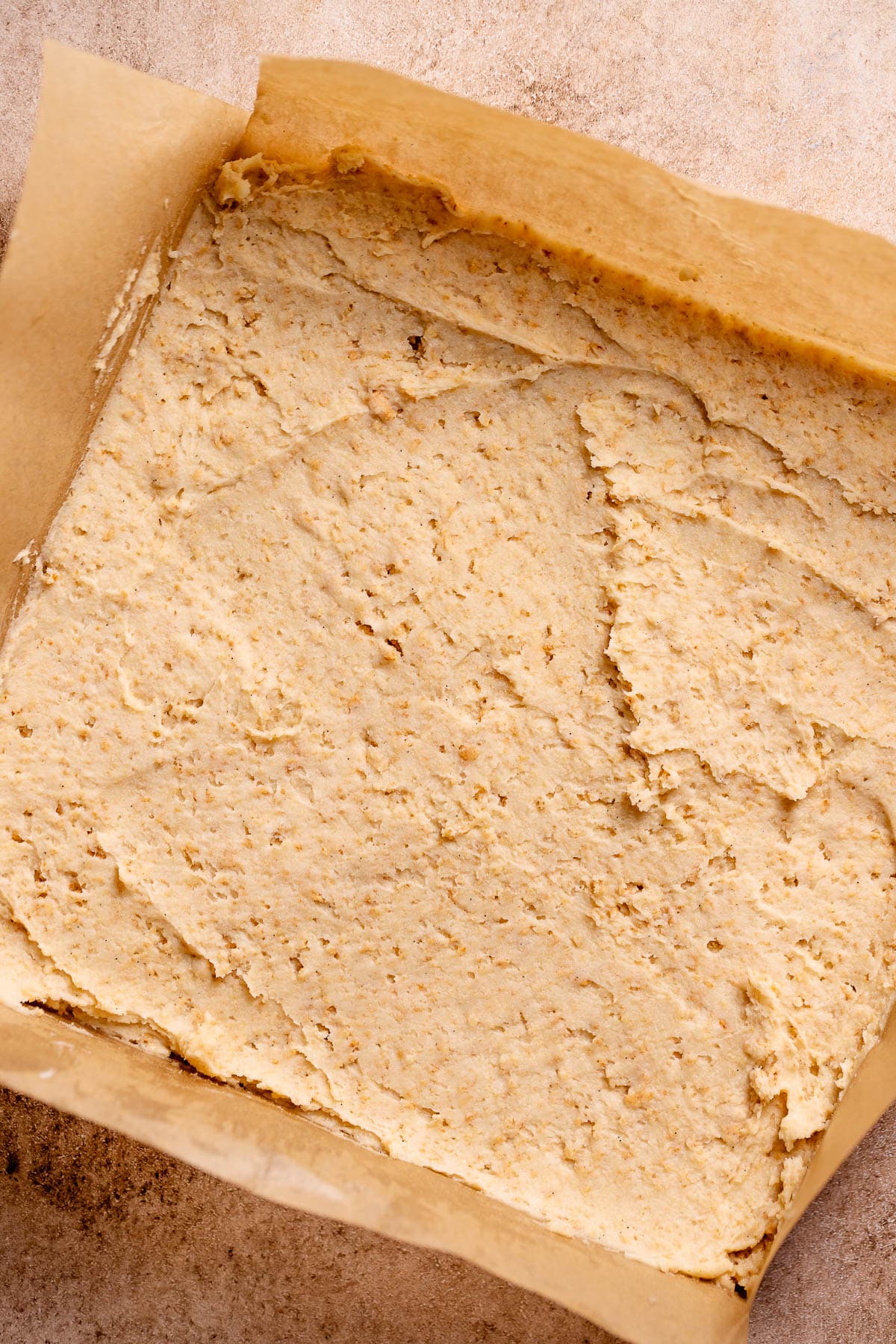 Graham cracker cookie dough spread onto parchment paper in a square shape.