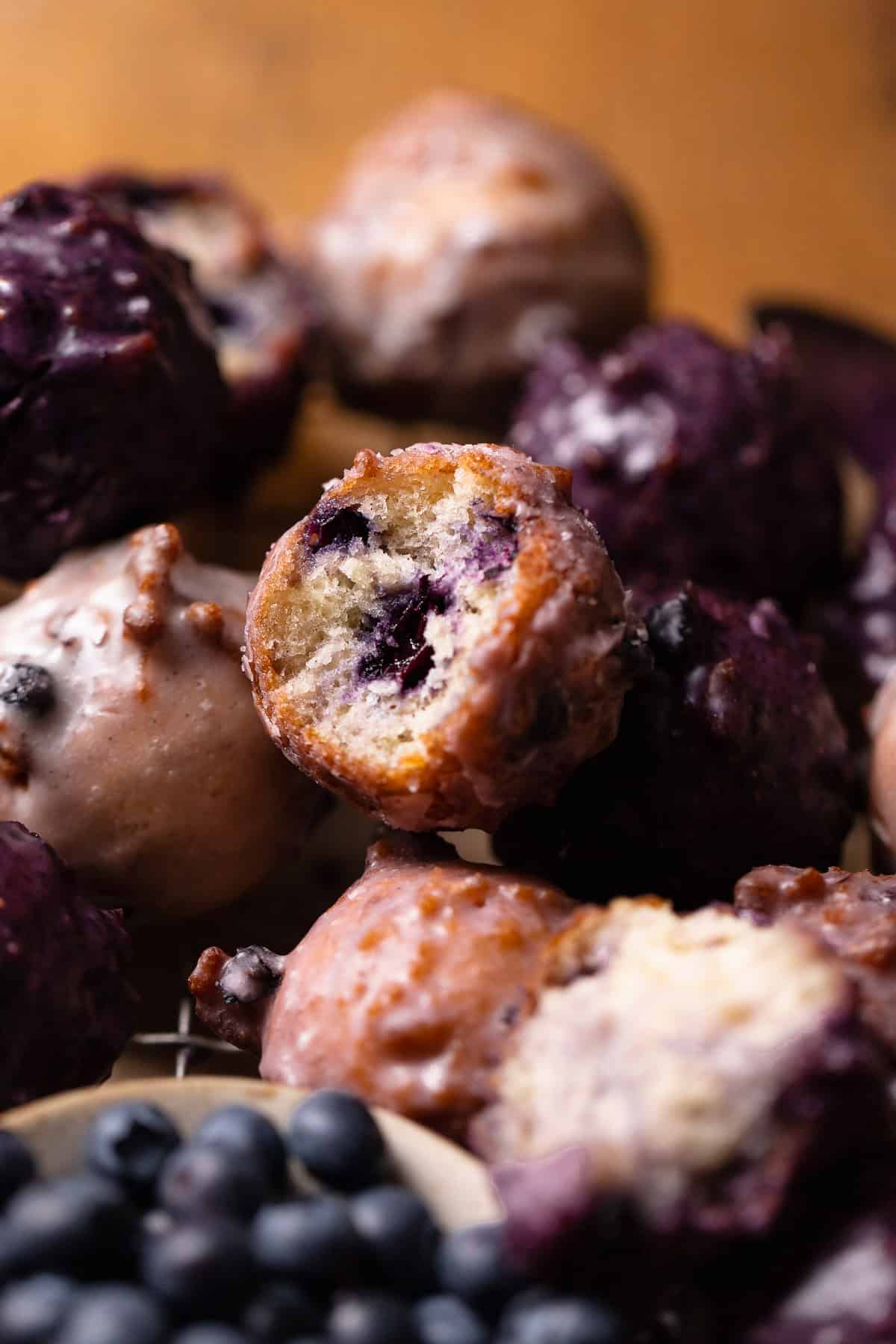A mini blueberry donut with a bite missing in a stack of other donuts.