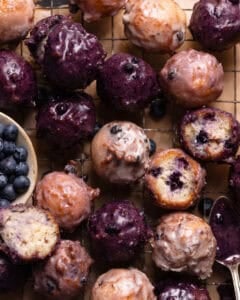 Close up shot of blueberry cake donuts with blueberry glaze on a wire rack.