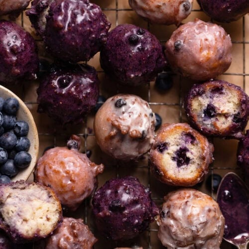 Close up shot of blueberry cake donuts with blueberry glaze on a wire rack.