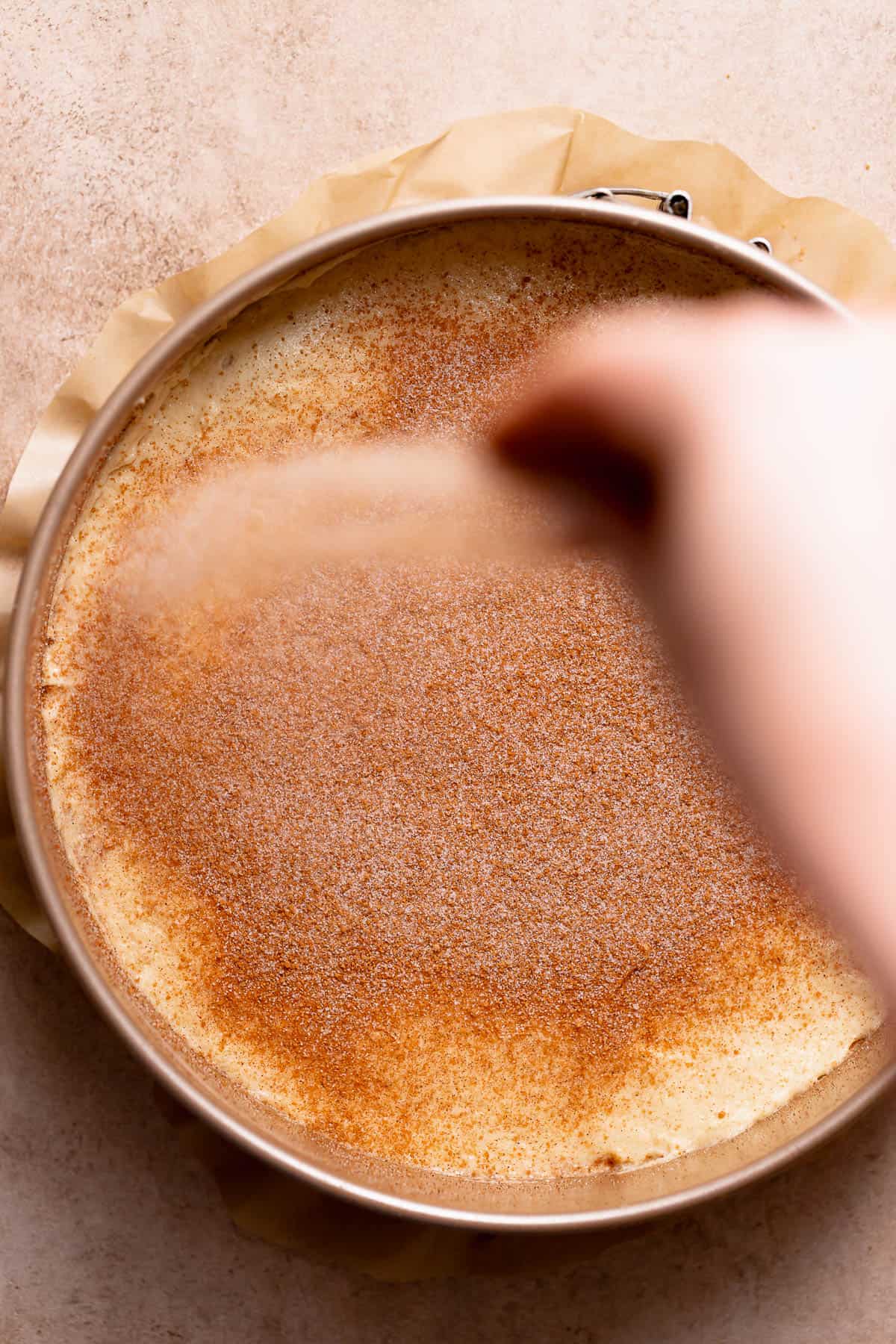 A hand covering the top of the cinnamon coffee cake with brown sugar cinnamon streusel.