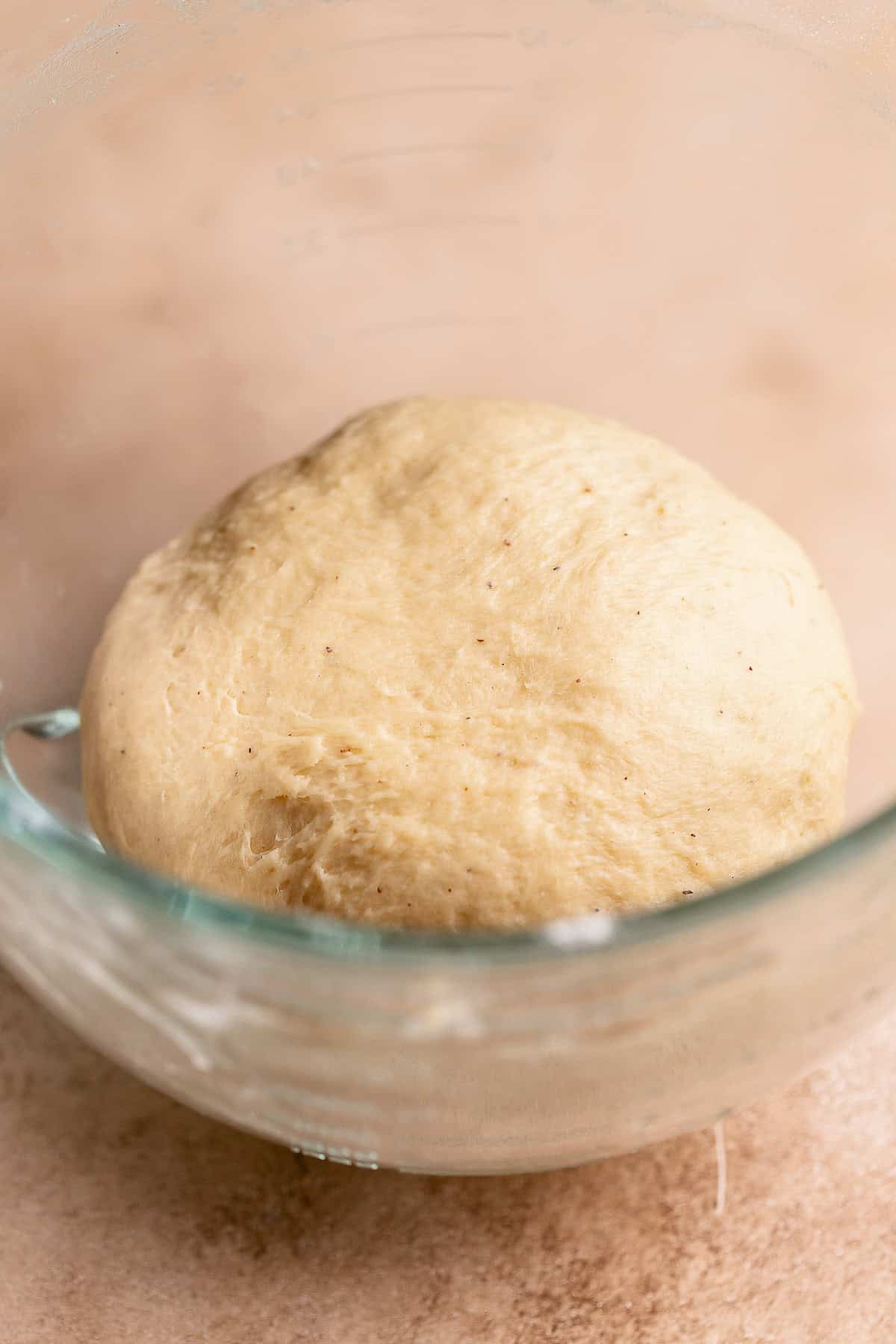 Cinnamon roll dough ball in a glass mixer bowl.