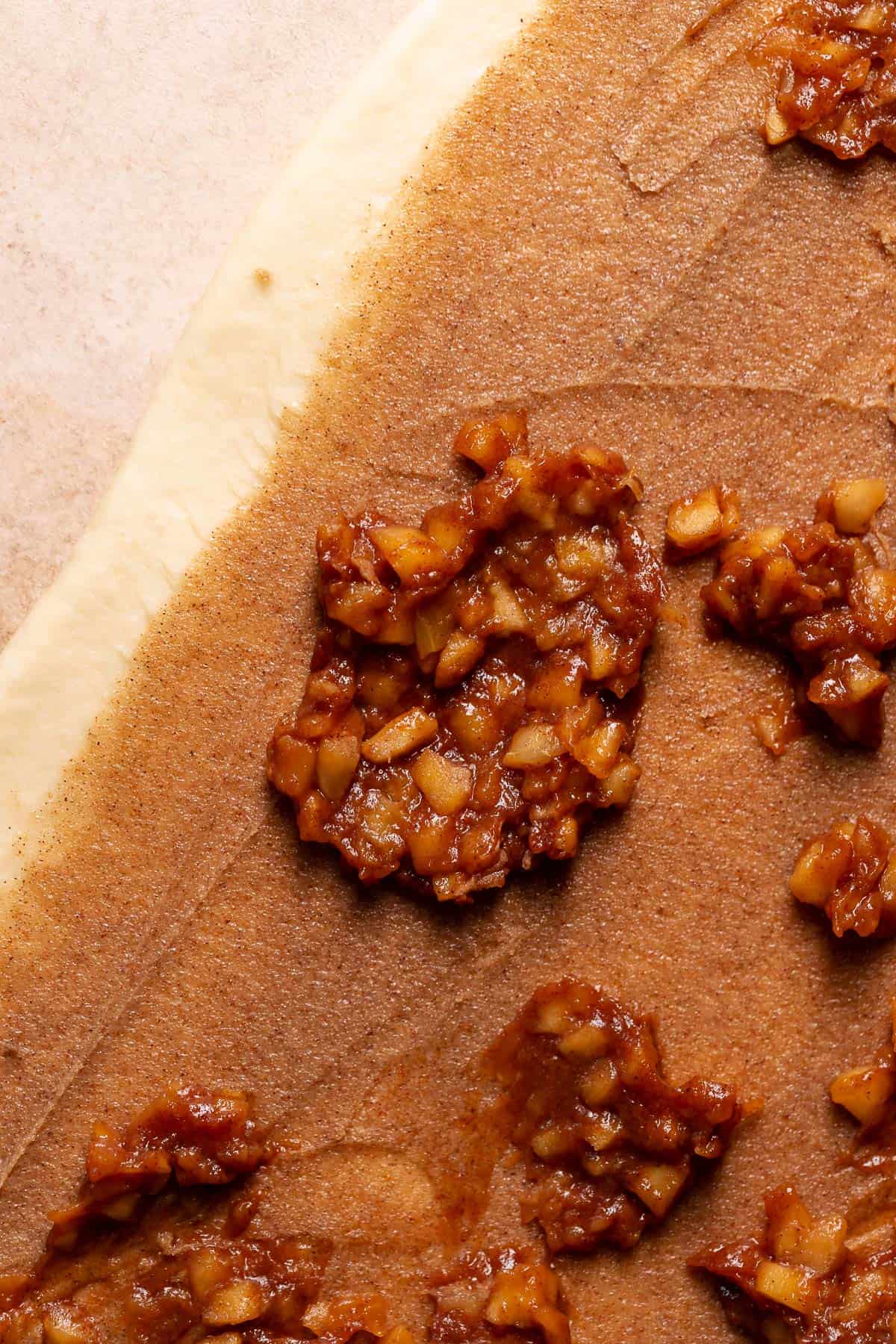 Apple filling being spread across the cinnamon sugar filling on the cinnamon roll dough.