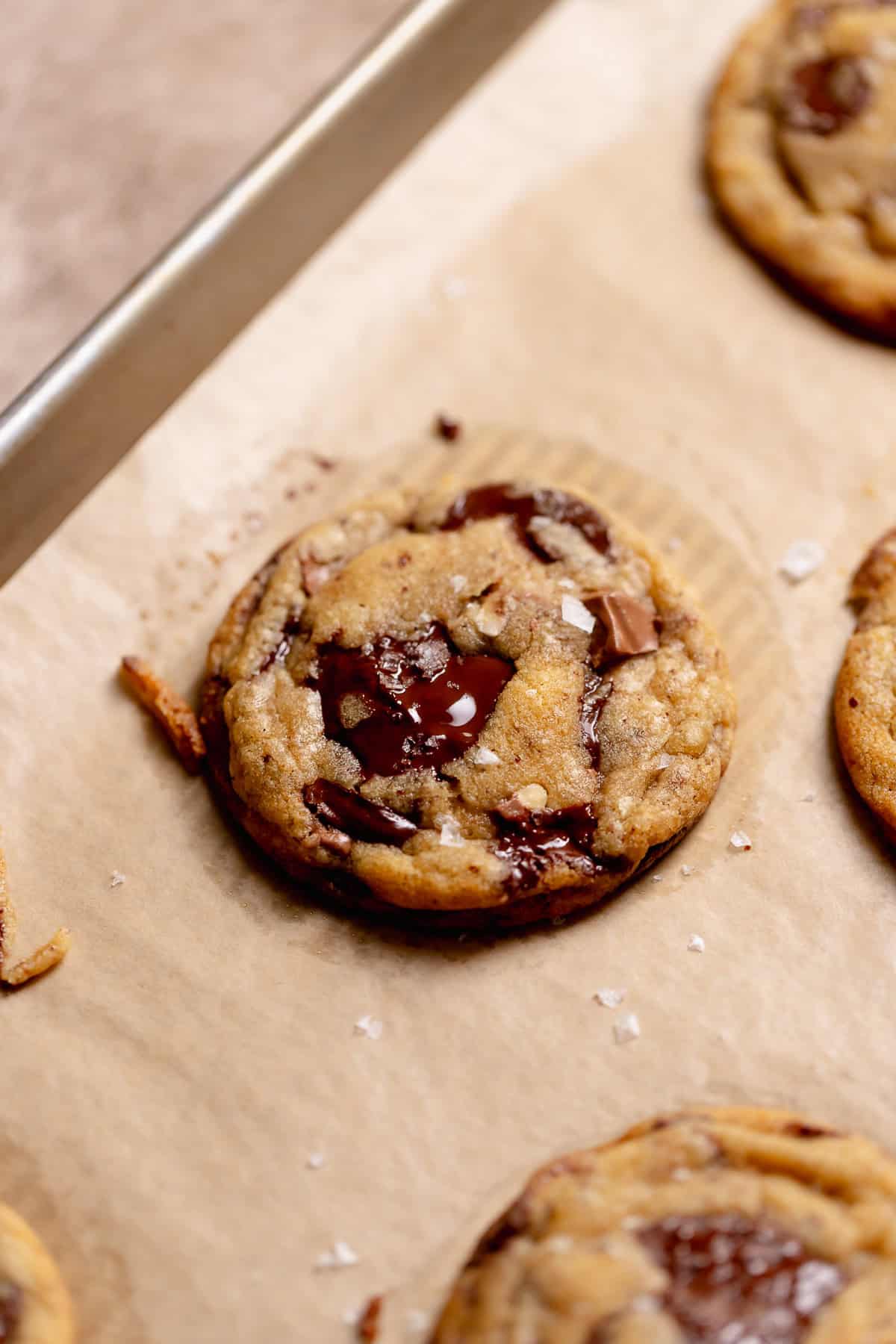 A brown butter cookie on a tray after baking sprinkled with flaky sea salt.