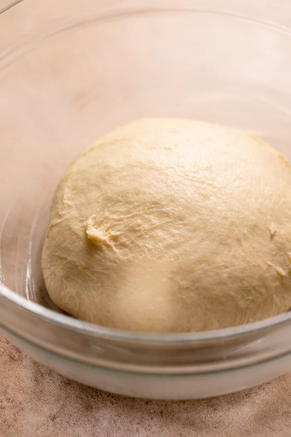 A smooth donut dough ball in a glass bowl.