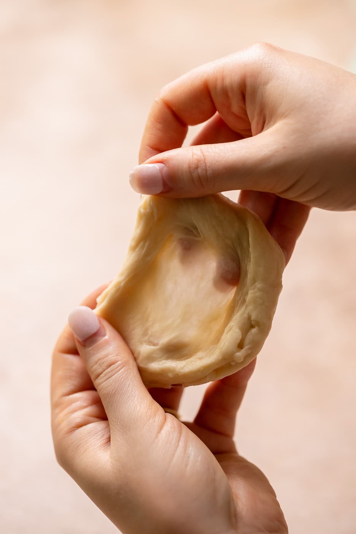 Two hands holding a piece of donut dough to show the gluten windowpane.
