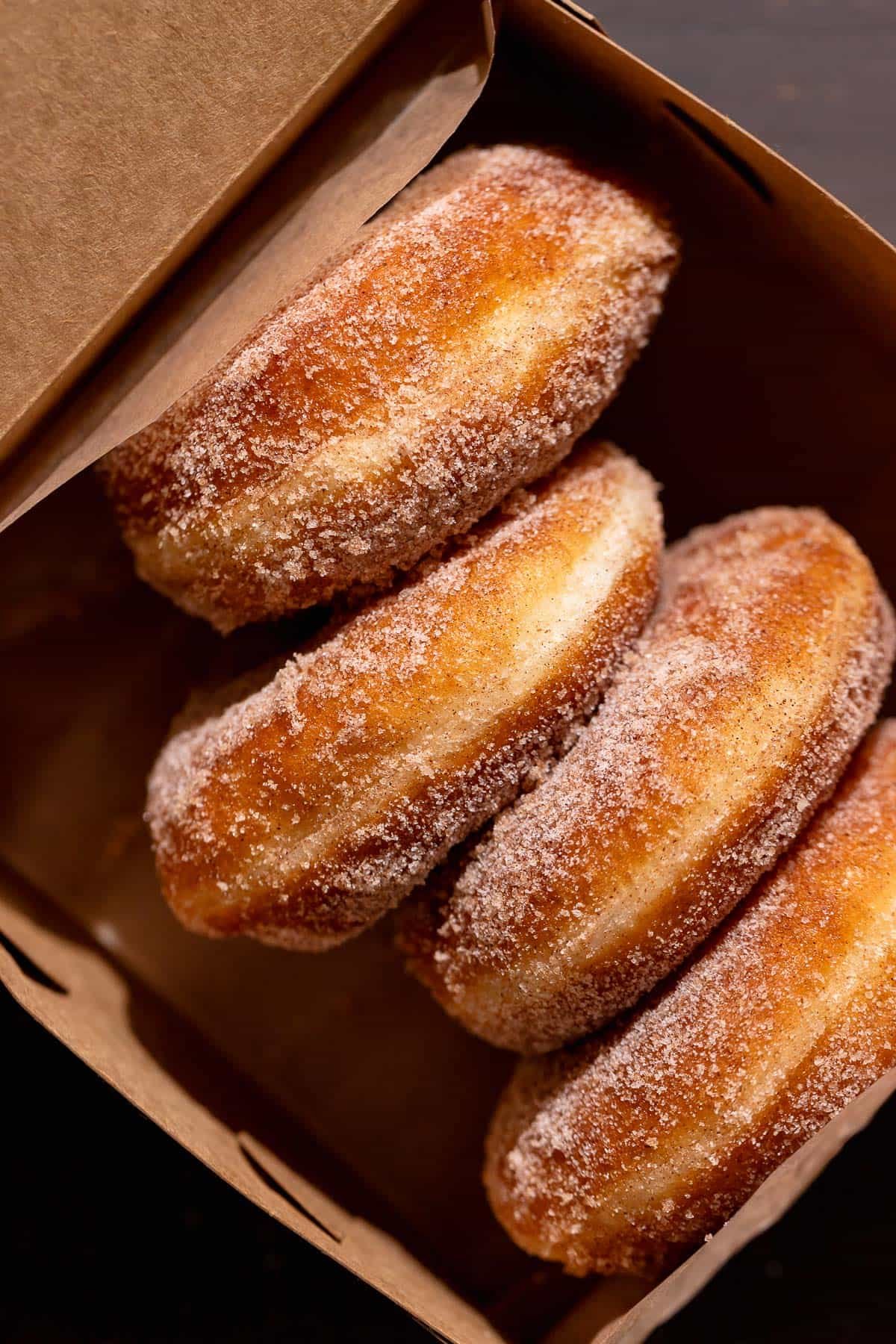 Four cinnamon sugar donuts in a brown paper box.