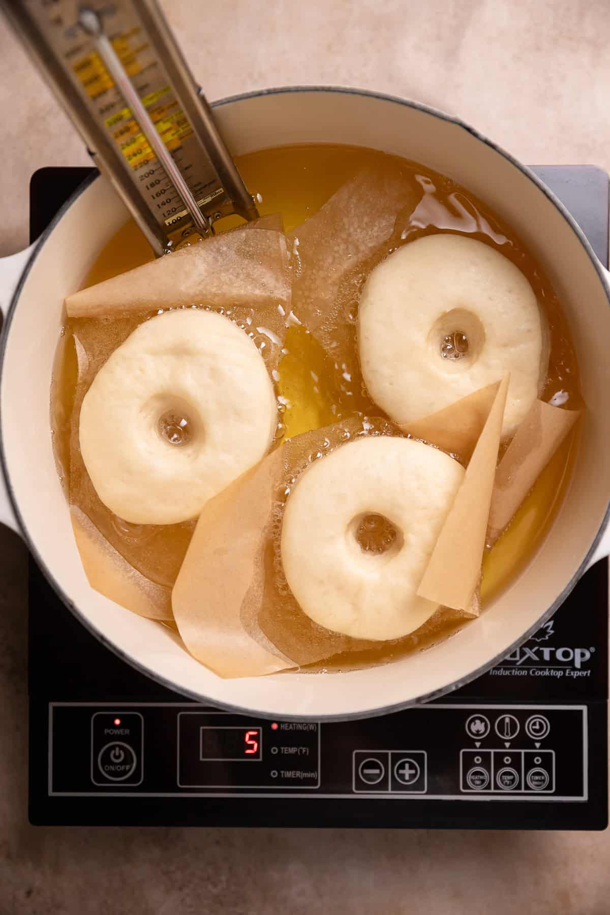 Three donuts frying in a pot of oil.
