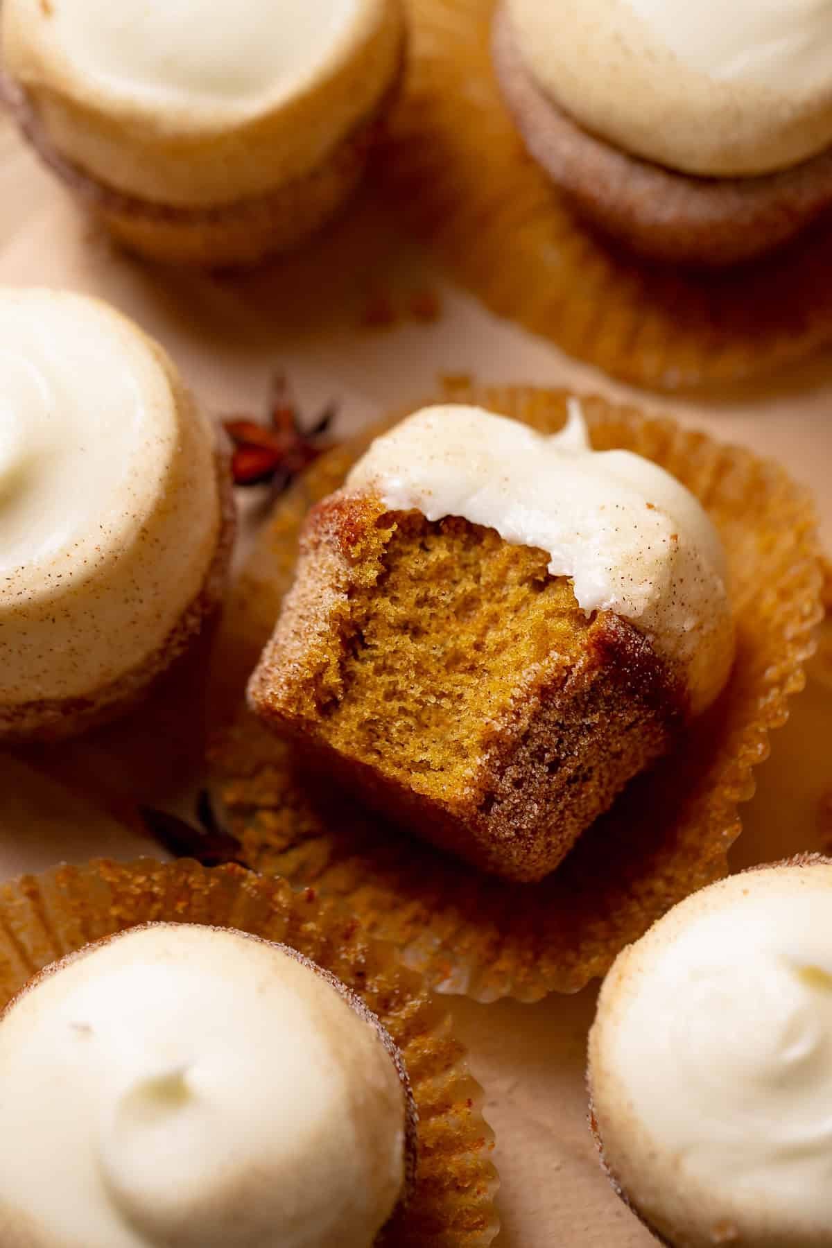 A pumpkin cupcake with cream cheese frosting on its side missing a bite.