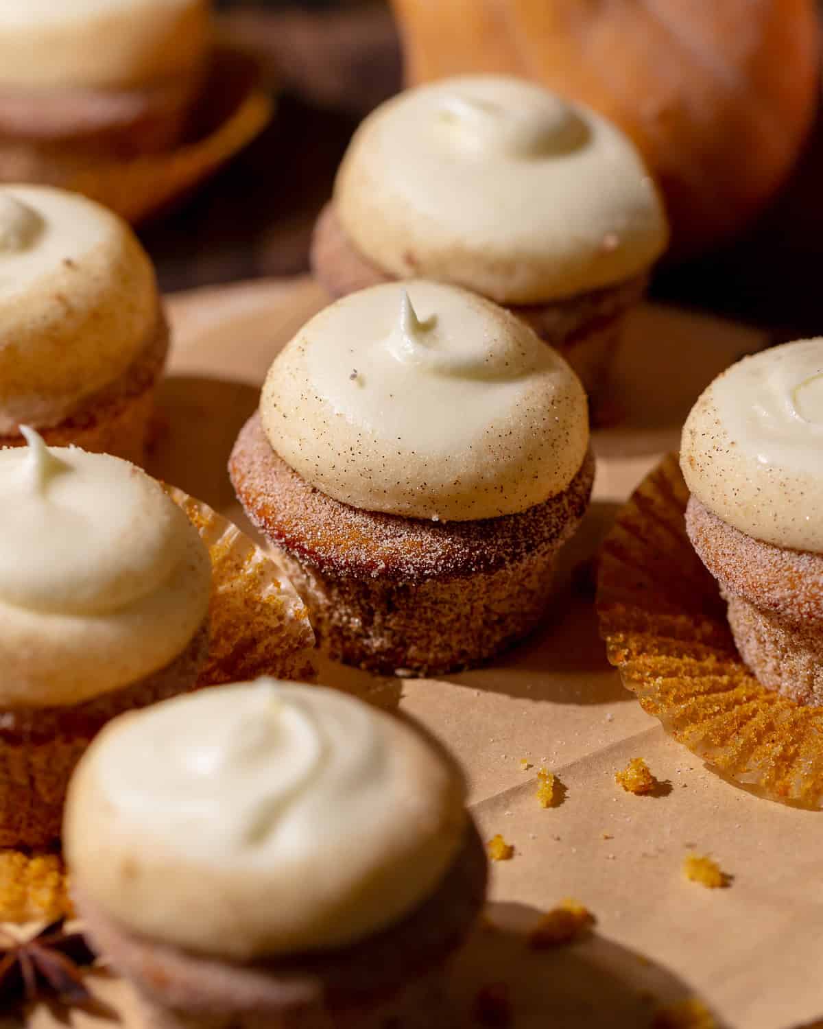 Pumpkin spice cupcakes with cream cheese icing on brown parchment paper.