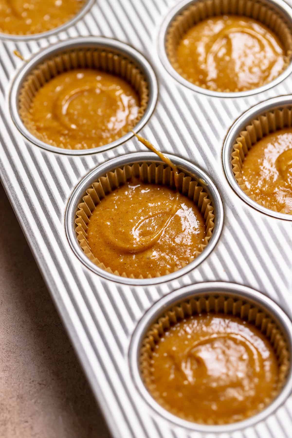 Pumpkin spice batter scooped into liners in a cupcake tray.
