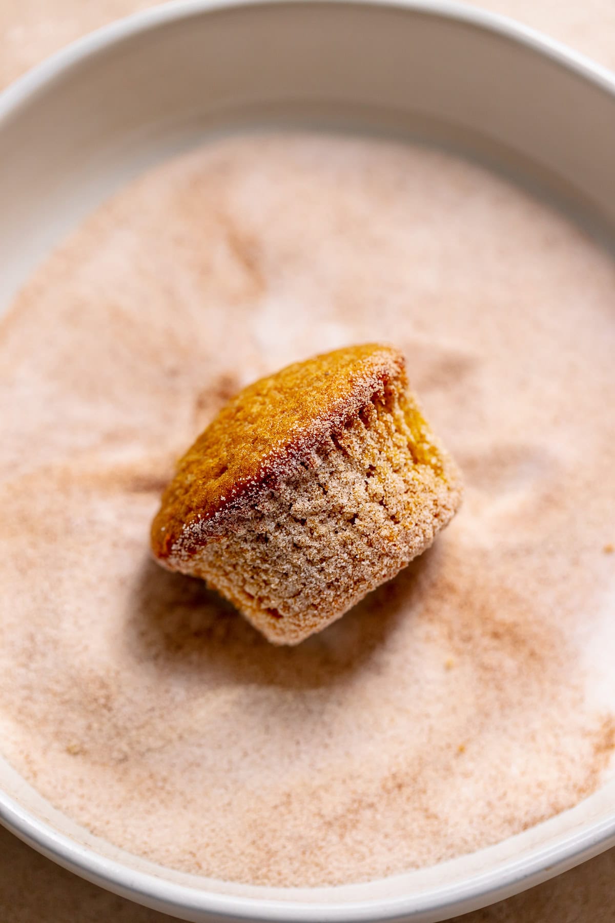 A pumpkin cupcake being rolled in spiced sugar.