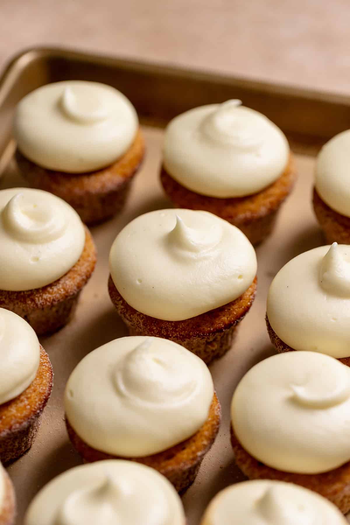 Cream cheese frosted pumpkin cupcakes on a baking tray.