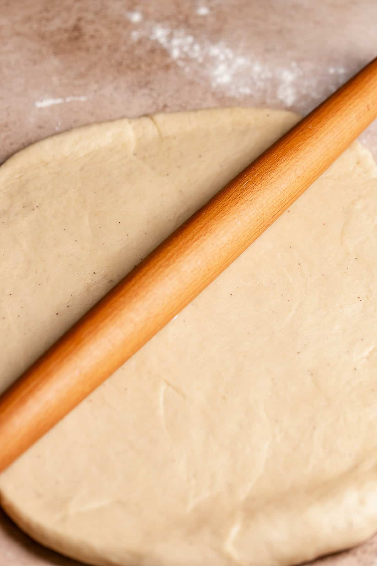 A rolling pin rolling out the apple bun dough.