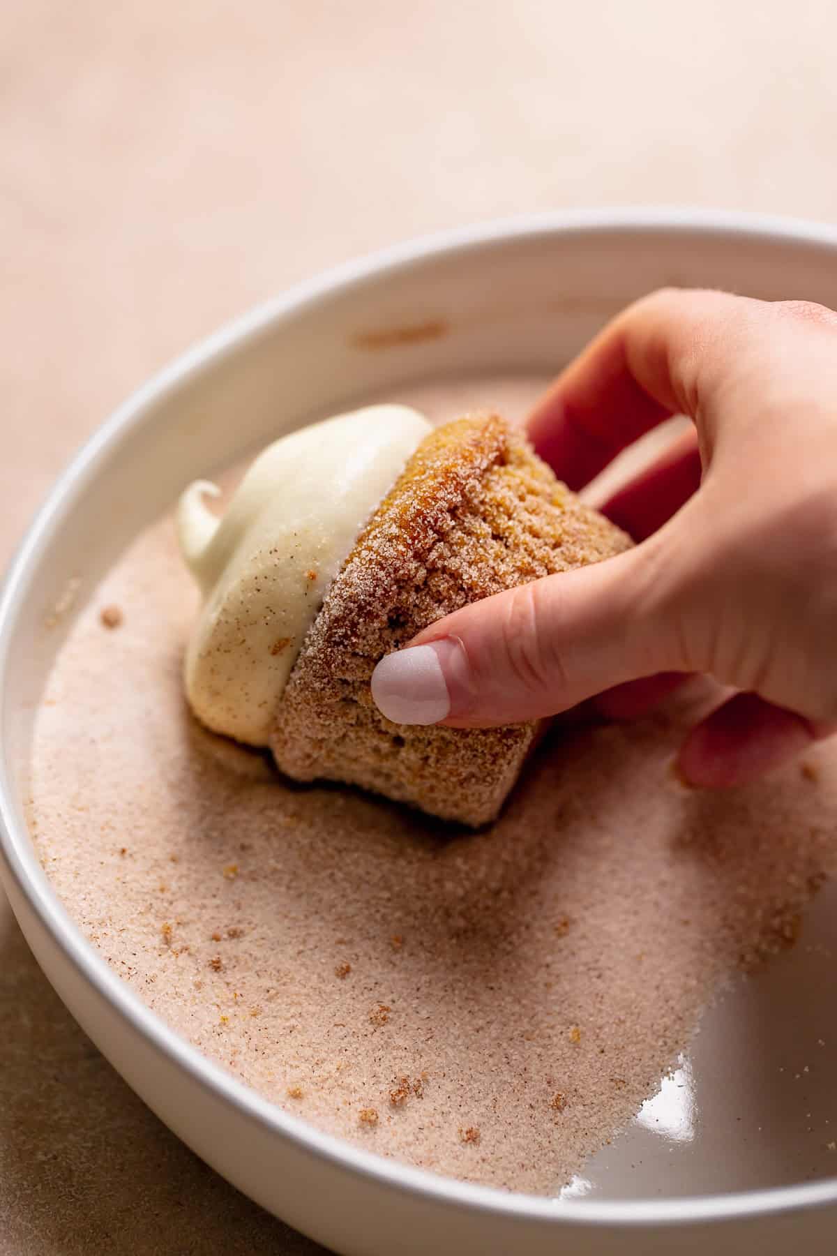 A hand rolling a pumpkin spice cupcake in sugar.