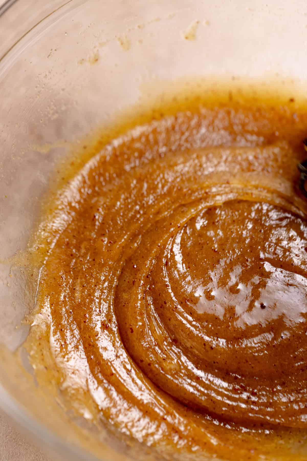 A glass bowl with the brown butter, sugar, and eggs being whisked together.