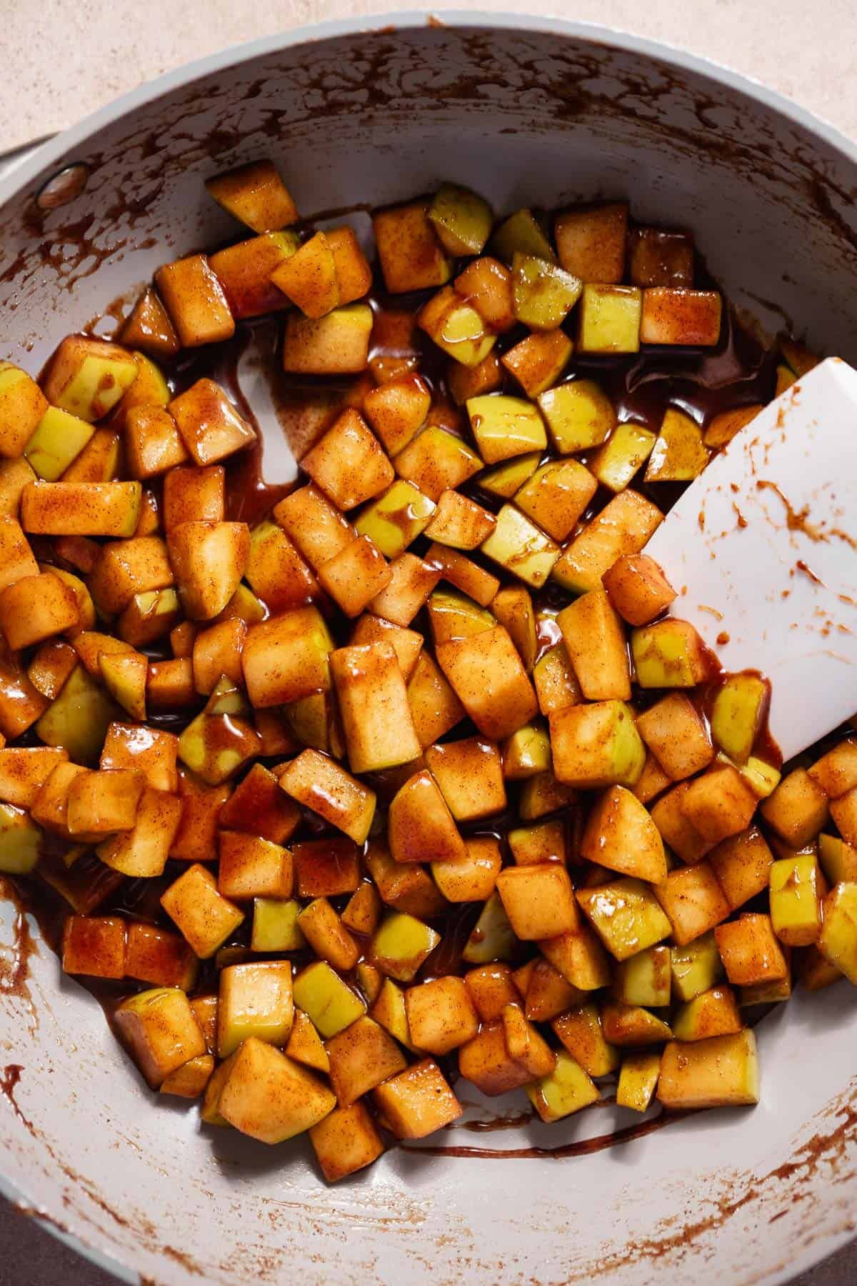 Cooked cinnamon sugar apples in a pan being stirred with a spatula.
