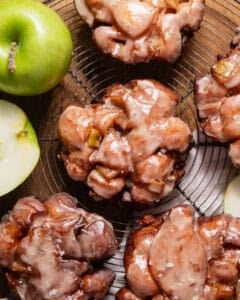 Deep fried apple fritters with apple cider glaze on a wire cooling rack.