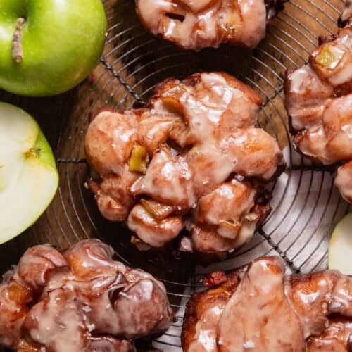 Deep fried apple fritters with apple cider glaze on a wire cooling rack.