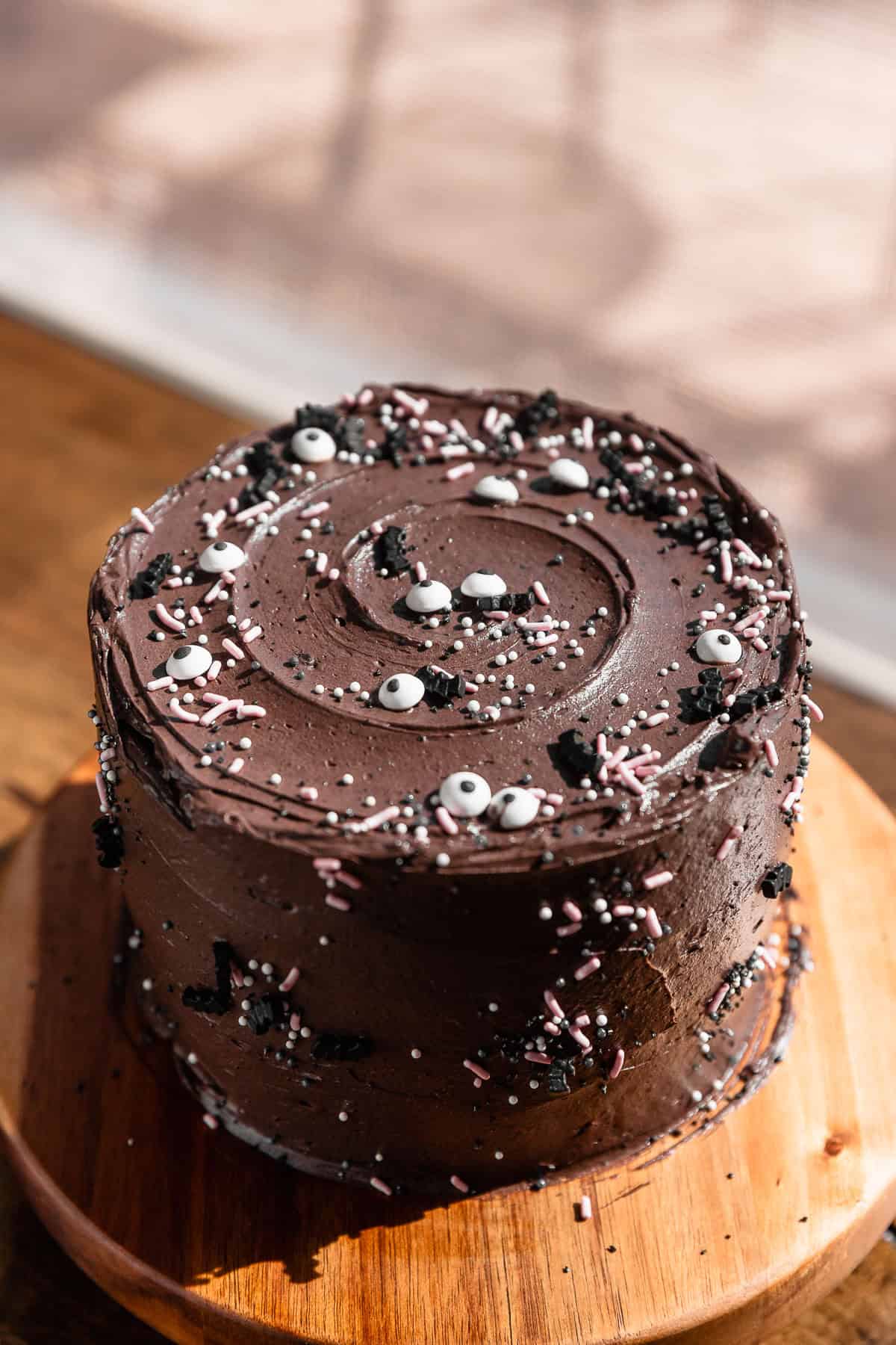 Chocolate velvet cake decorated with halloween sprinkles on a wooden cake stand.