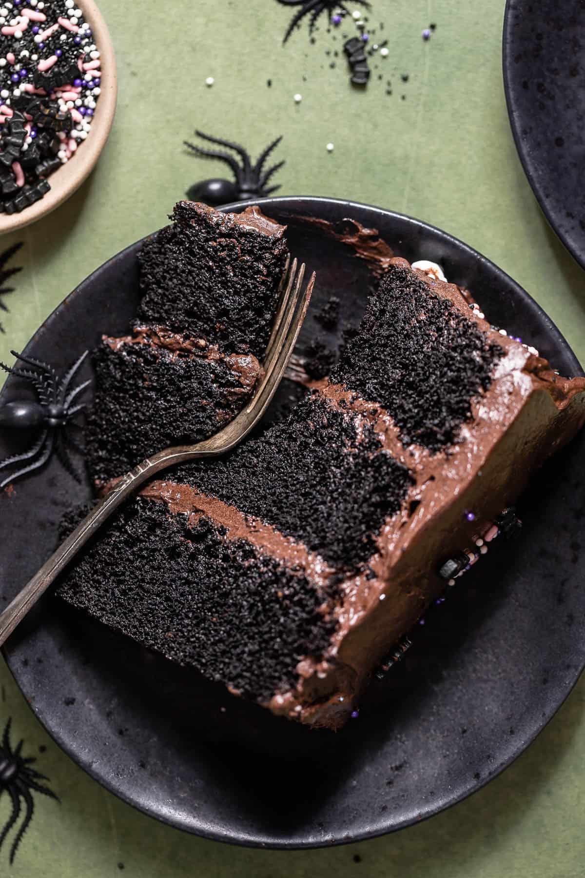 A slice of black cocoa cake on a black plate with a fork digging in.