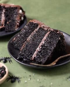 Slice of black velvet cake with black cocoa buttercream on a black plate.