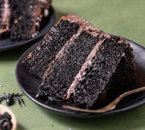 Slice of black velvet cake with black cocoa buttercream on a black plate.