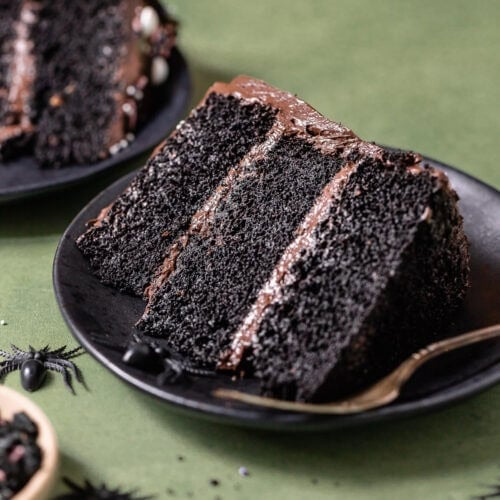 Slice of black velvet cake with black cocoa buttercream on a black plate.