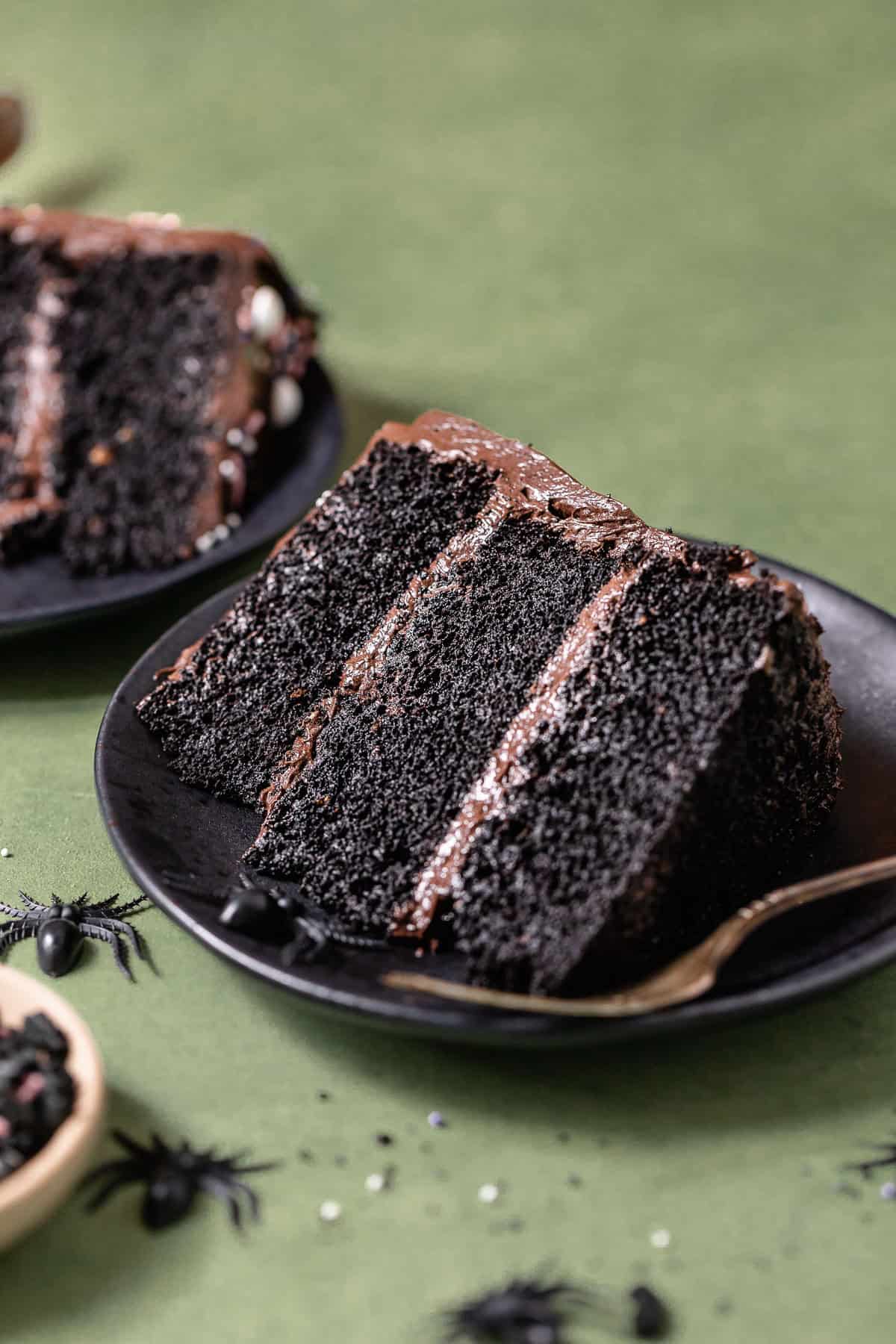 A slice of black velvet cake with black cocoa frosting on a black plate.
