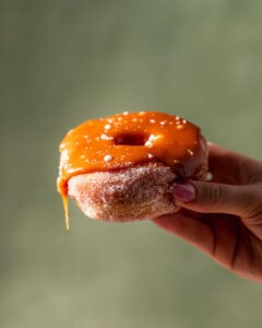 A hand holding a donut covered in salted caramel thats dripping off one of the sides.