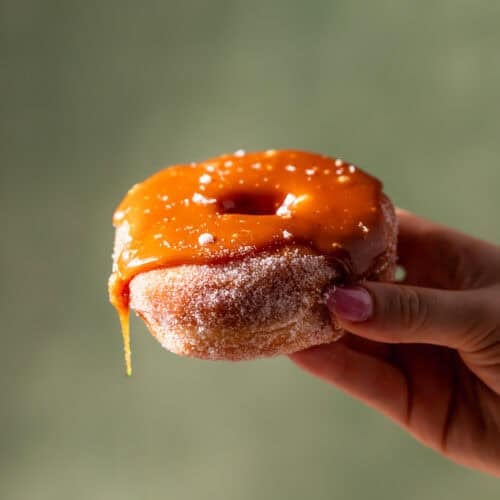 A hand holding a donut covered in salted caramel thats dripping off one of the sides.