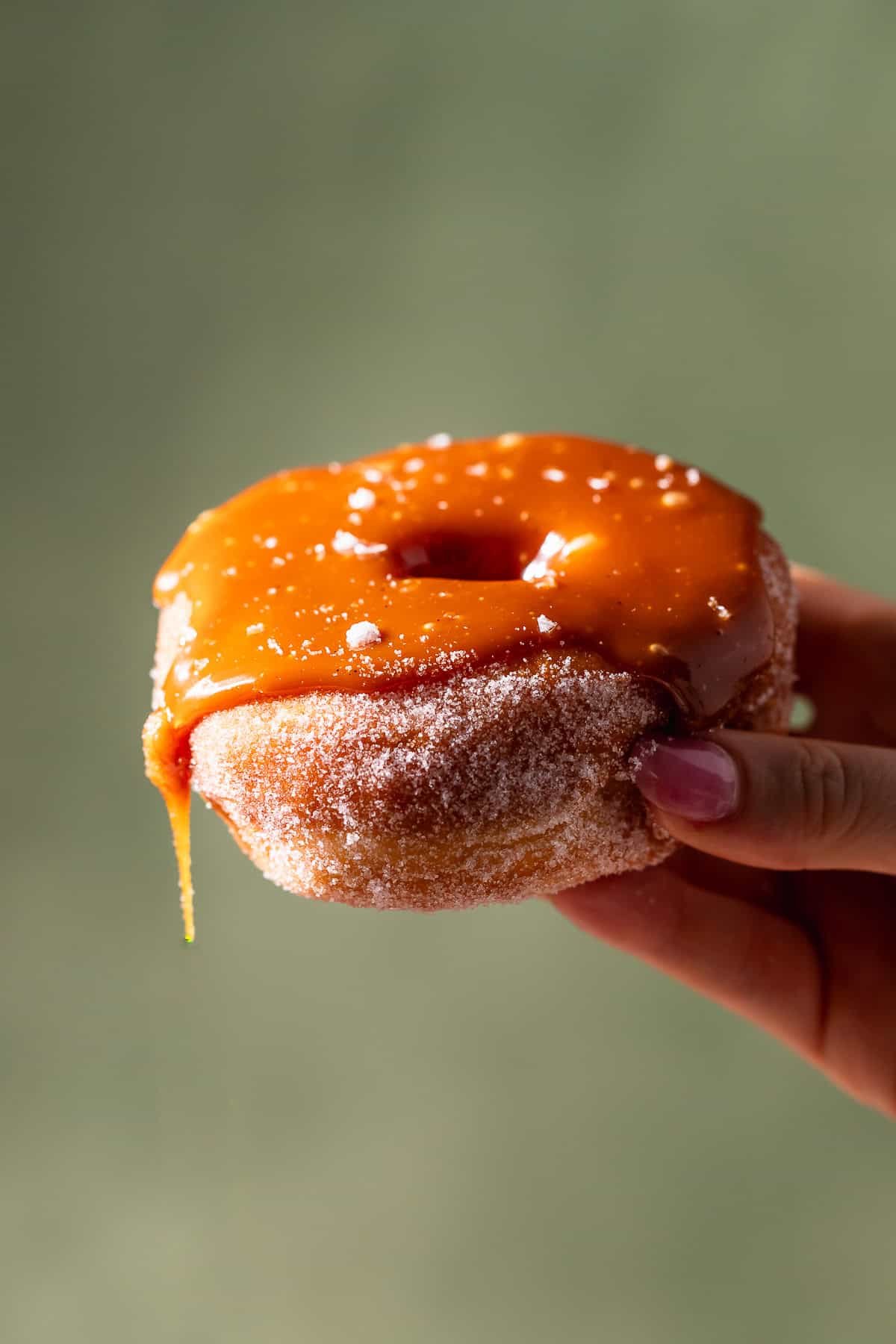 A hand holding a donut with caramel dripping off the side.