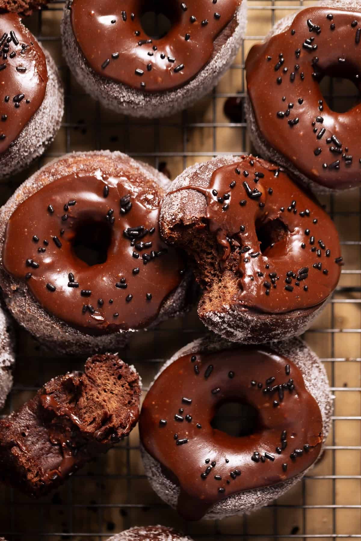 Chocolate frosted donuts with chocolate sprinkles on a wire baking rack.