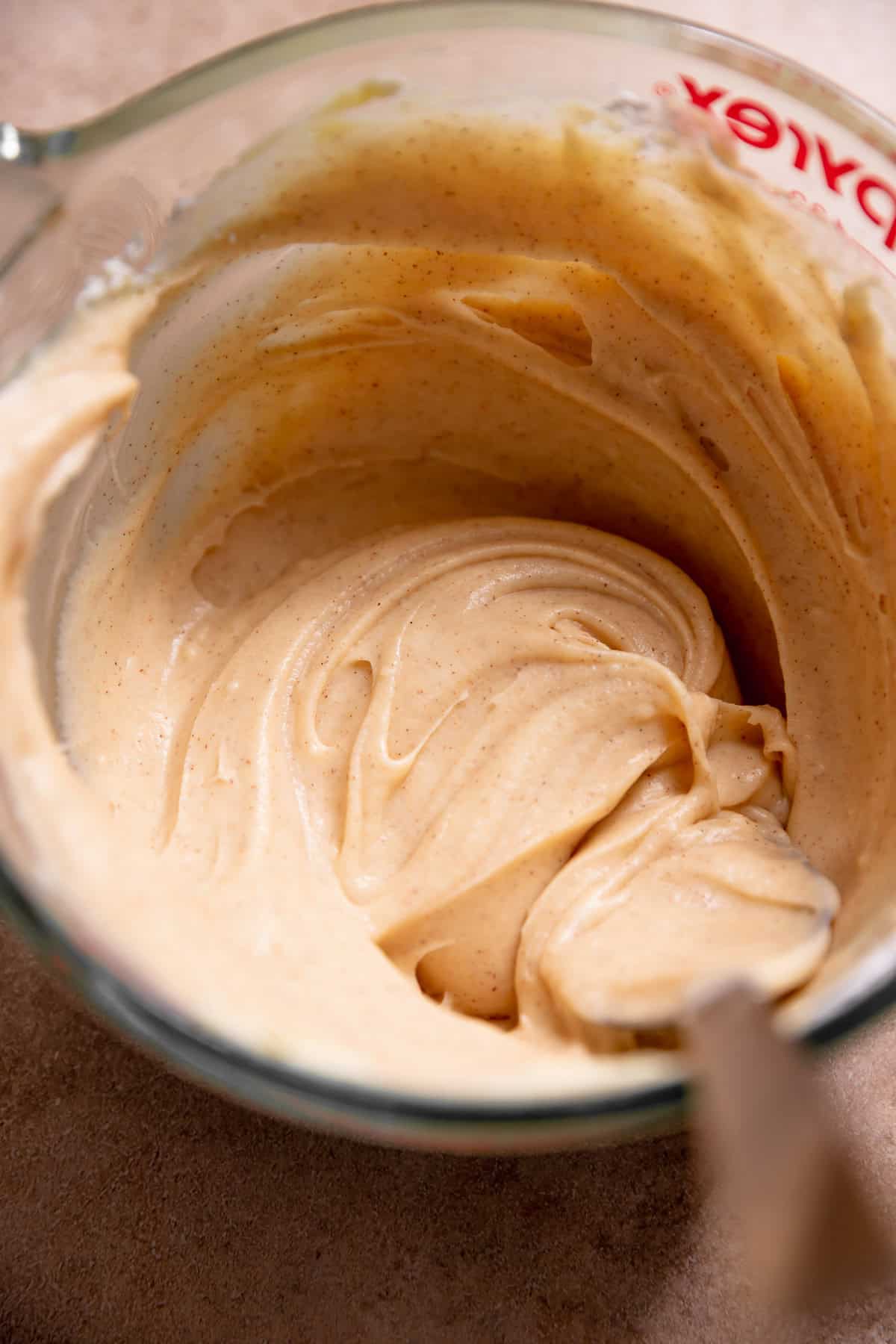 Cinnamon cream cheese frosting for the tops of the cinnamon rolls in a glass measuring cup.