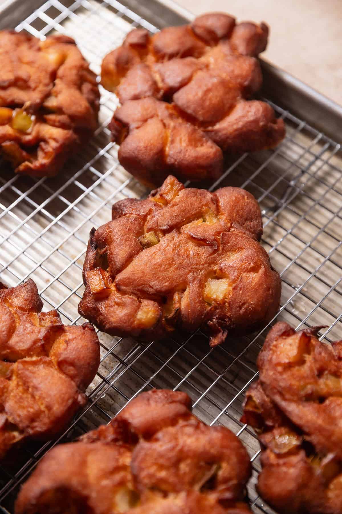 Deep fried apple fritters cooling on a wire rack.