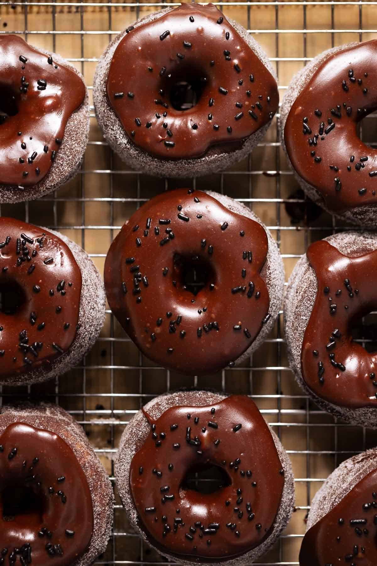 Chocolate donuts with chocolate frosting and chocolate sprinkles on a wire rack.