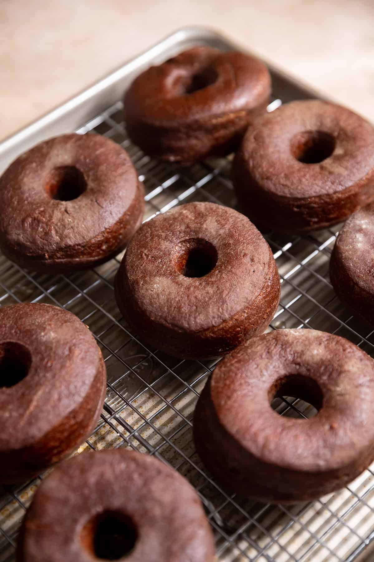 Fried chocolate donuts on a wire rack before frosting.