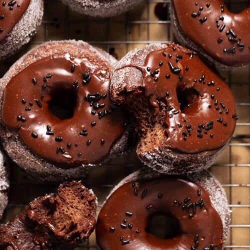 Double chocolate donuts with chocolate frosting and sprinkles on a wire rack.