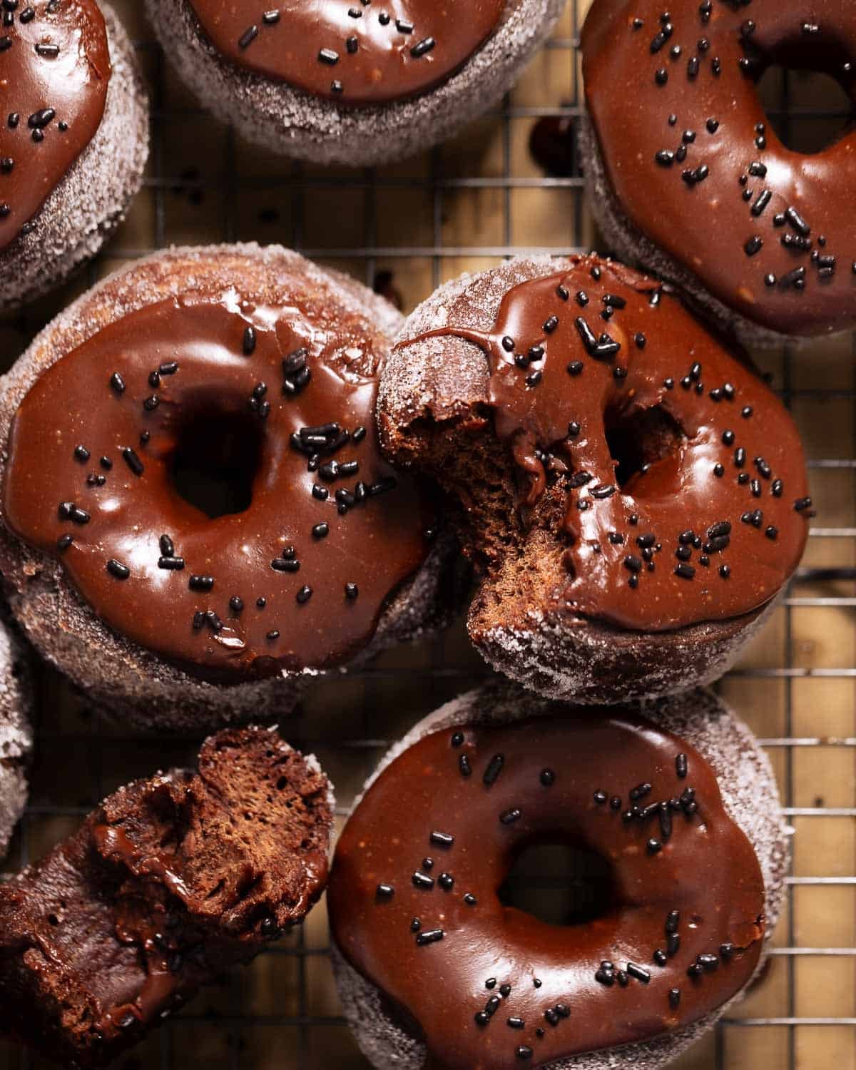 Double chocolate donuts with chocolate frosting and sprinkles on a wire rack.