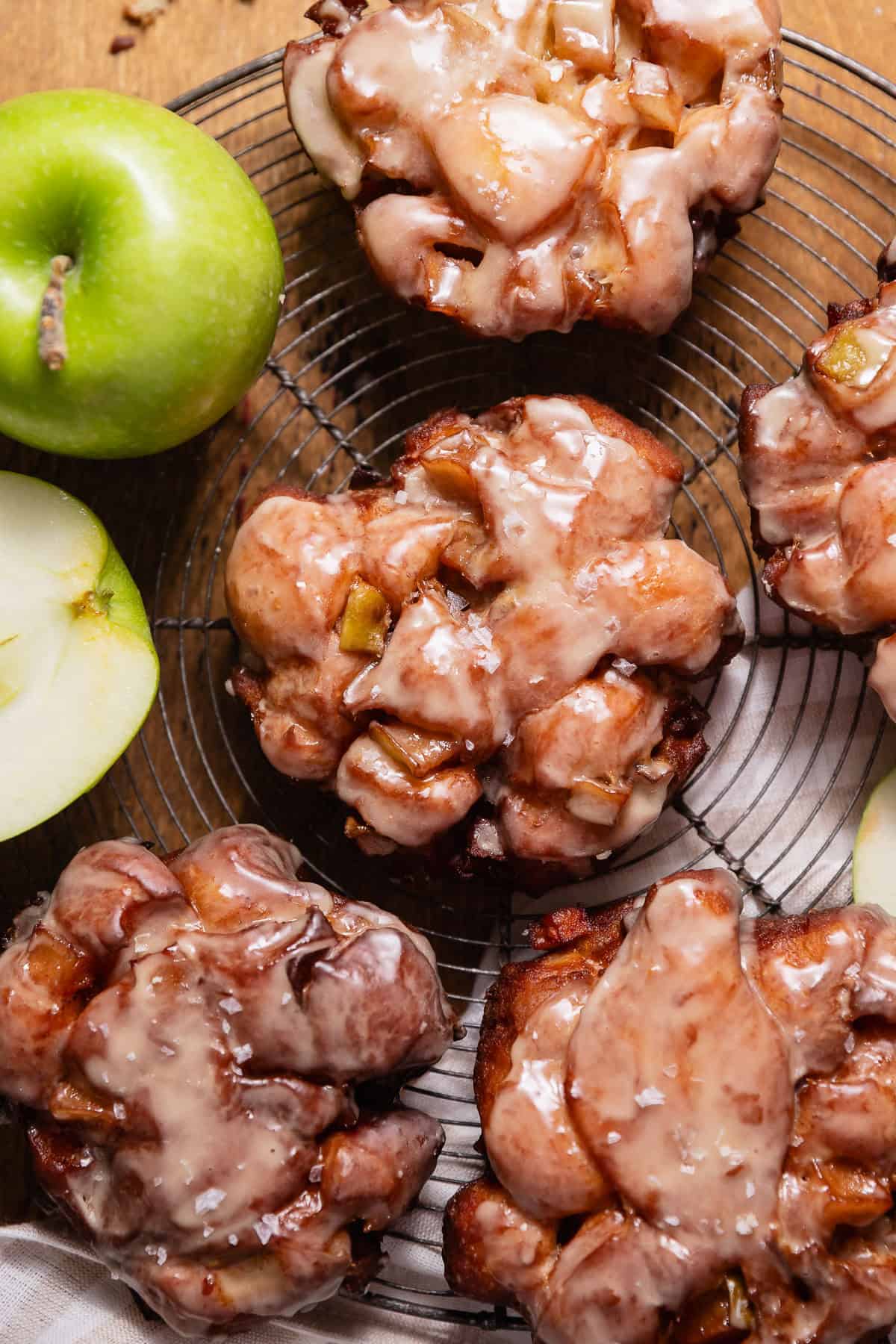 Glazed apple fritters sprinkled with flaky sea salt on a wire cooling rack.