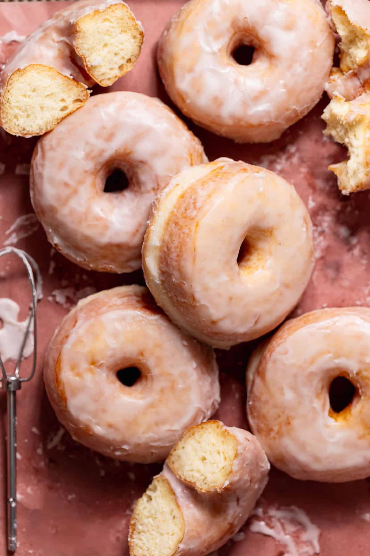 Glazed doughnuts on parchment paper with a few ripped in half to show the soft texture.