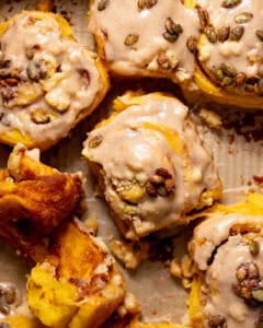 Pumpkin spice rolls filled with pumpkin pie filling in a baking pan being pulled apart.