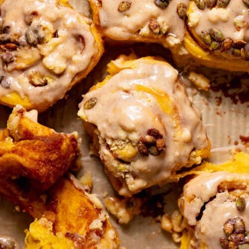 Pumpkin spice rolls filled with pumpkin pie filling in a baking pan being pulled apart.