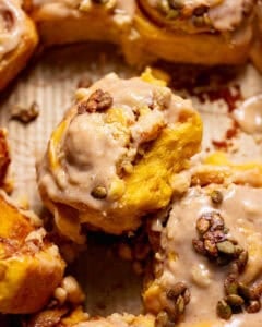 Pumpkin cinnamon rolls with cinnamon cream cheese frosting and candied pumpkin seeds in a baking pan.
