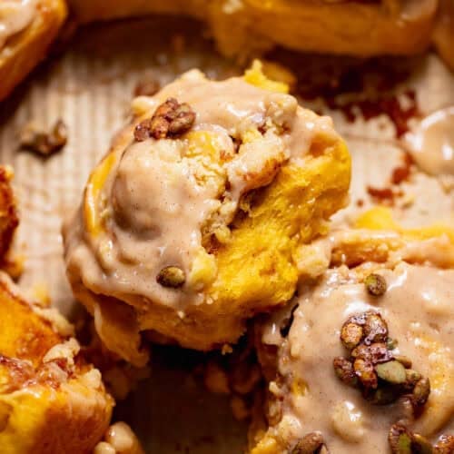Pumpkin cinnamon rolls with cinnamon cream cheese frosting and candied pumpkin seeds in a baking pan.