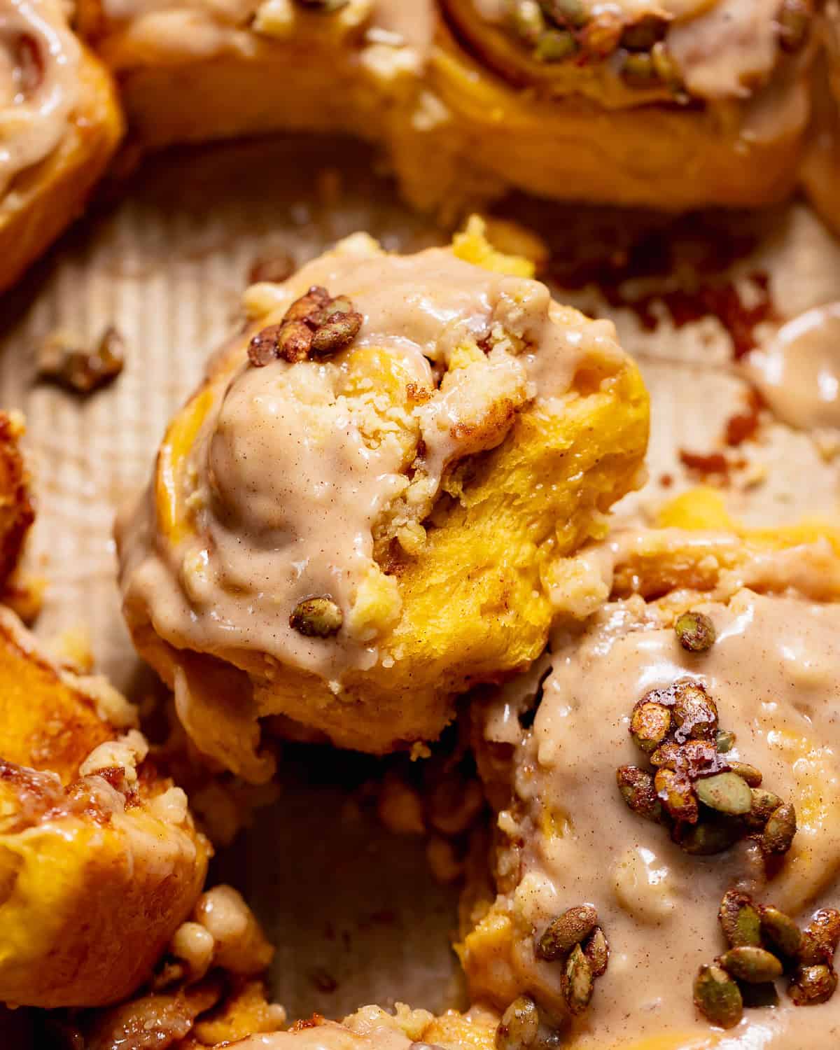 Pumpkin cinnamon rolls with cinnamon cream cheese frosting and candied pumpkin seeds in a baking pan.